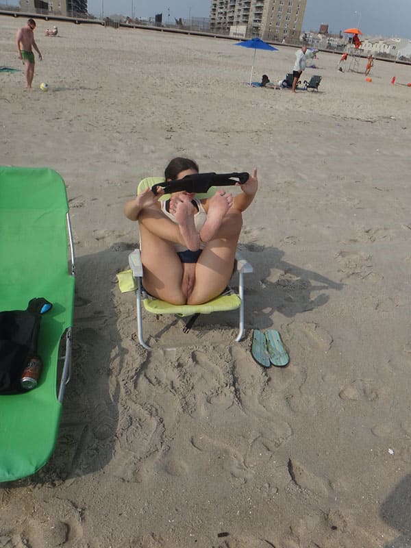 Жена на пляжном стуле задрав ноги вверх пытается надеть на голую пизду плавки