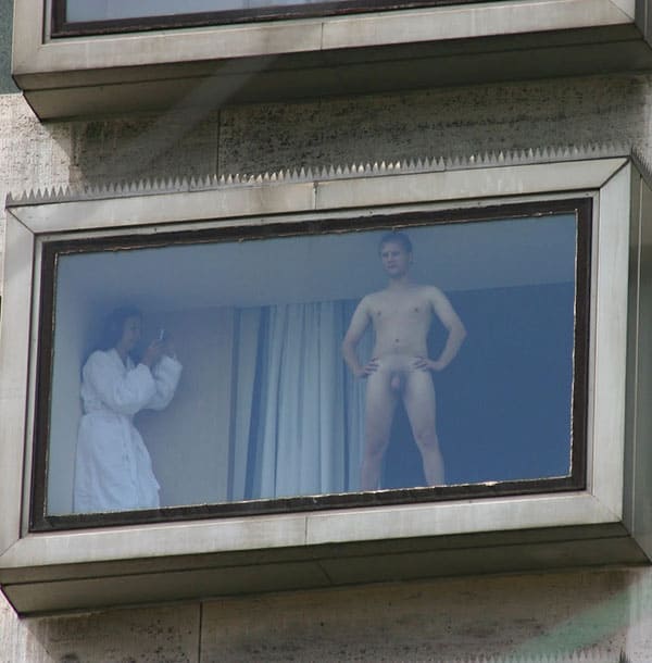 Жена в белом халате фотографирует голого мужа перед окном в гостиничном номере