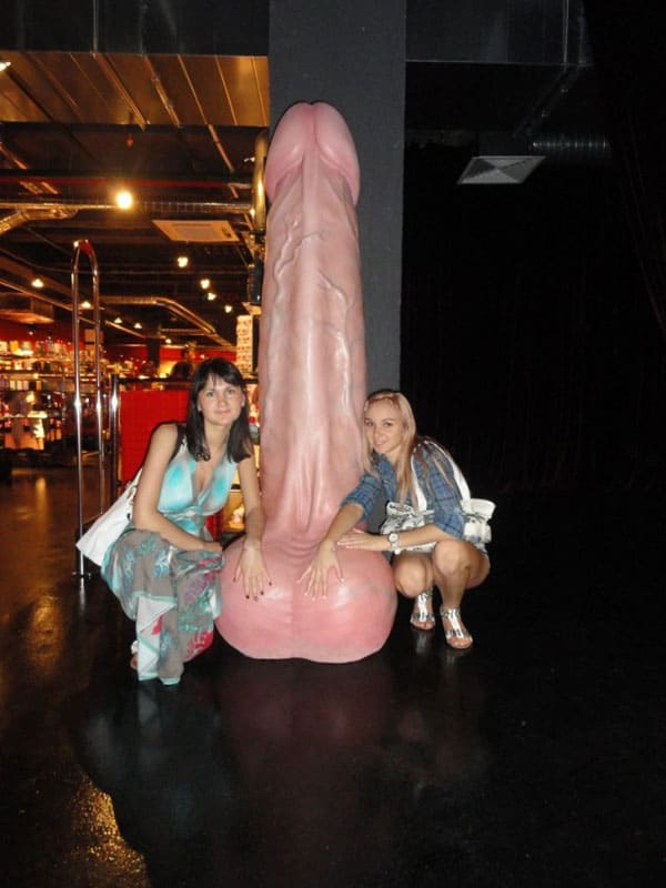 Две подруги фотографируются в секс-шопе со статуей в виде гигантского розового члена