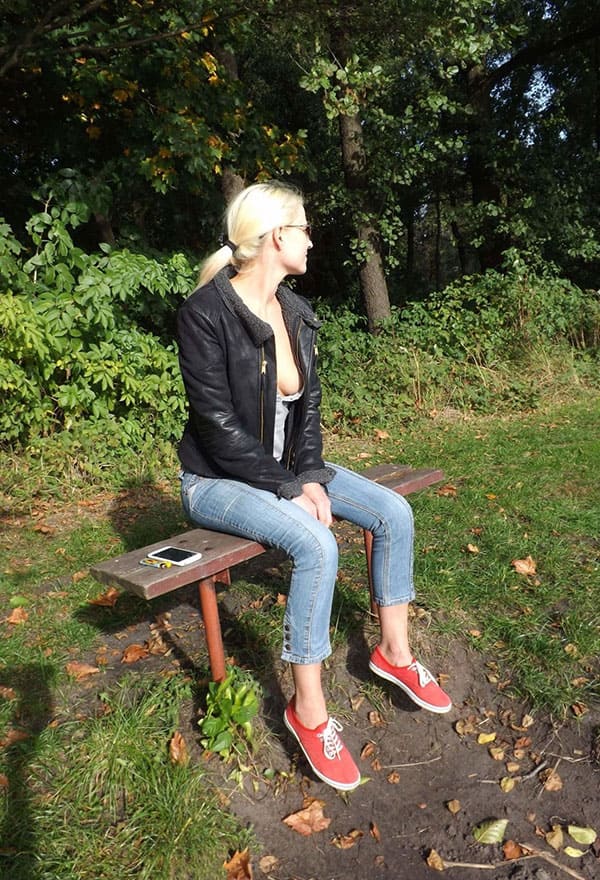 Блондинка сидит на скамейке в парке в футболке с глубоким вырезом