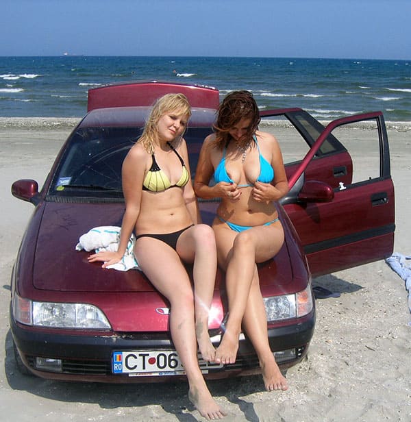 Подружки в купальниках сидят на капоте машины на берегу моря