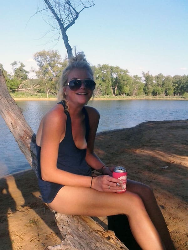 Девушка пьет пиво на берегу реки с соском торчащим из летней майки
