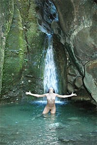 Молодая нудистка купается под водопадом